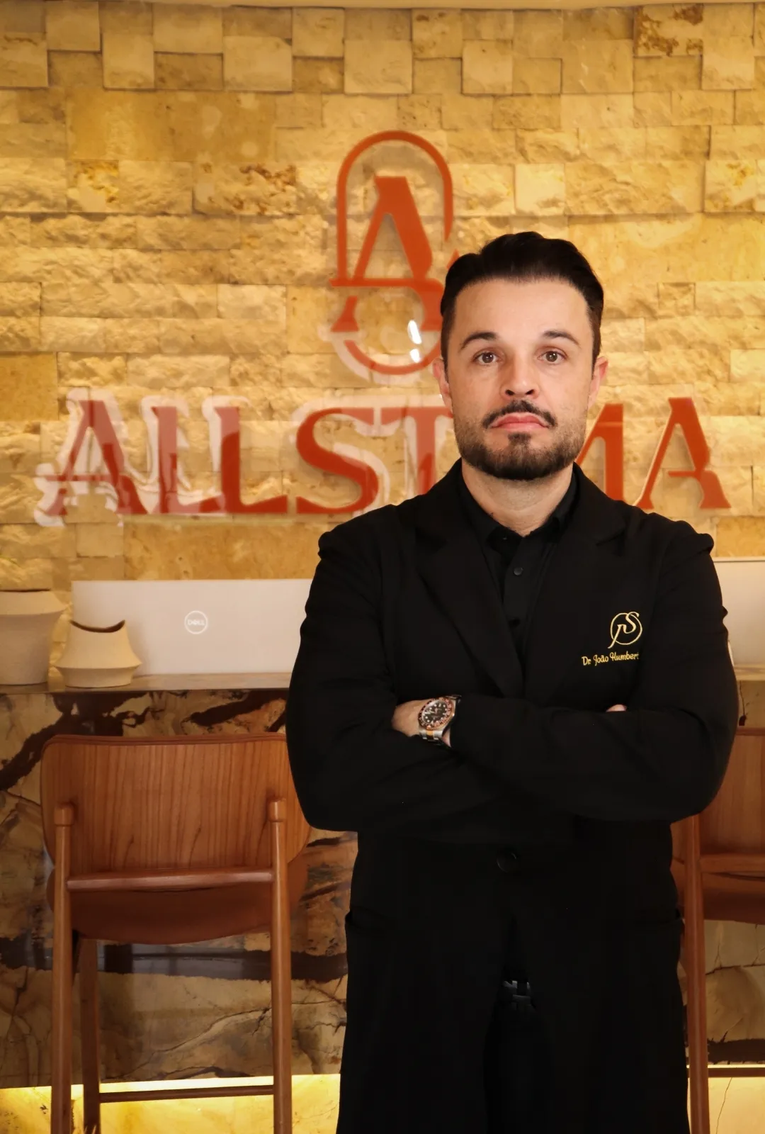 Dr. João Salgado na recepção da clínica Allstima, com parede de pedra ao fundo